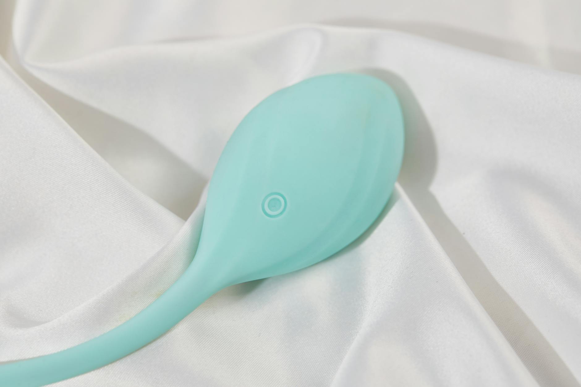 A teal-colored lemon clitoral vibrator resting on soft white silk fabric