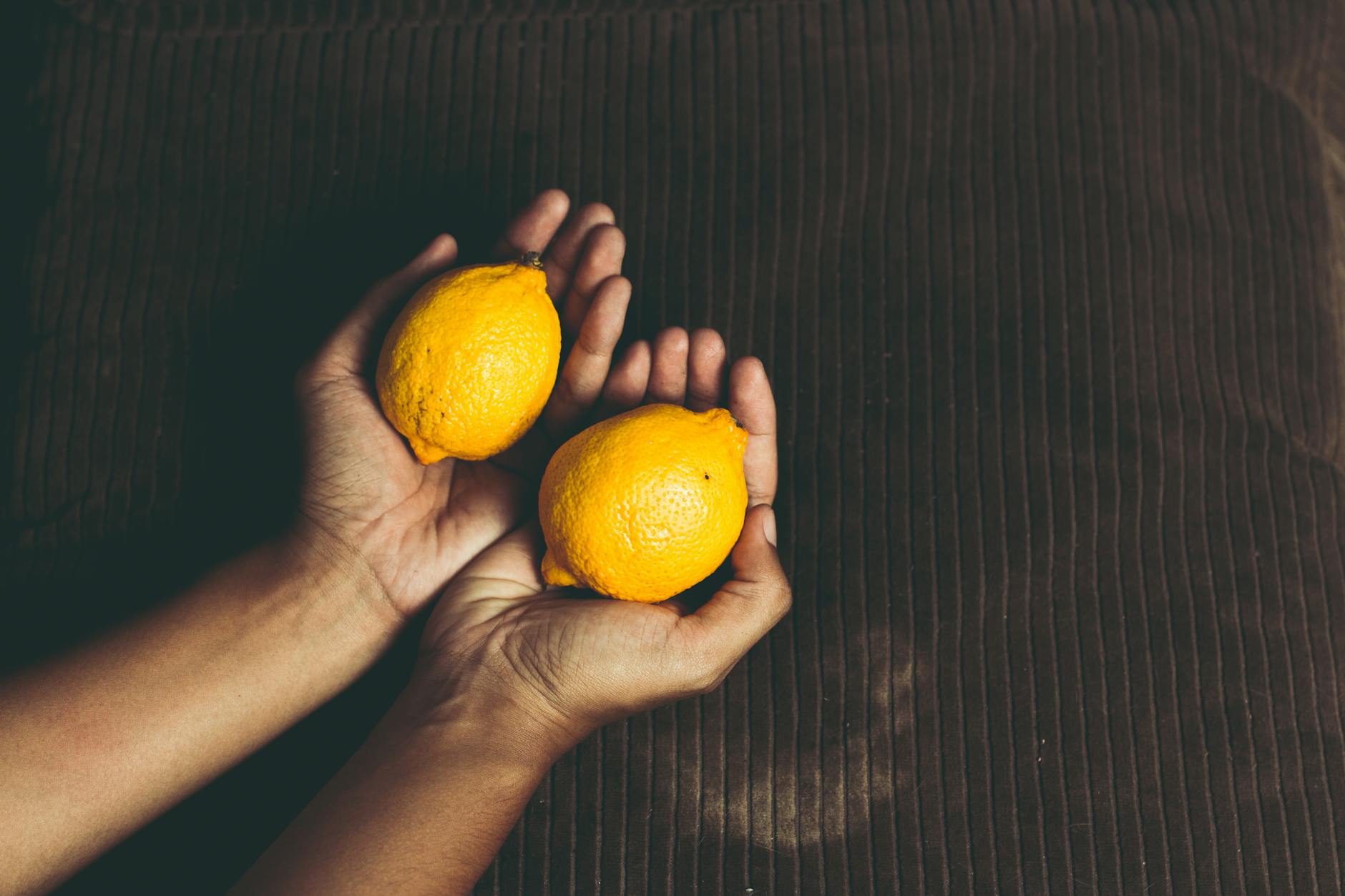 Hand holding an orange vibrator against a minimalistic purple backdrop