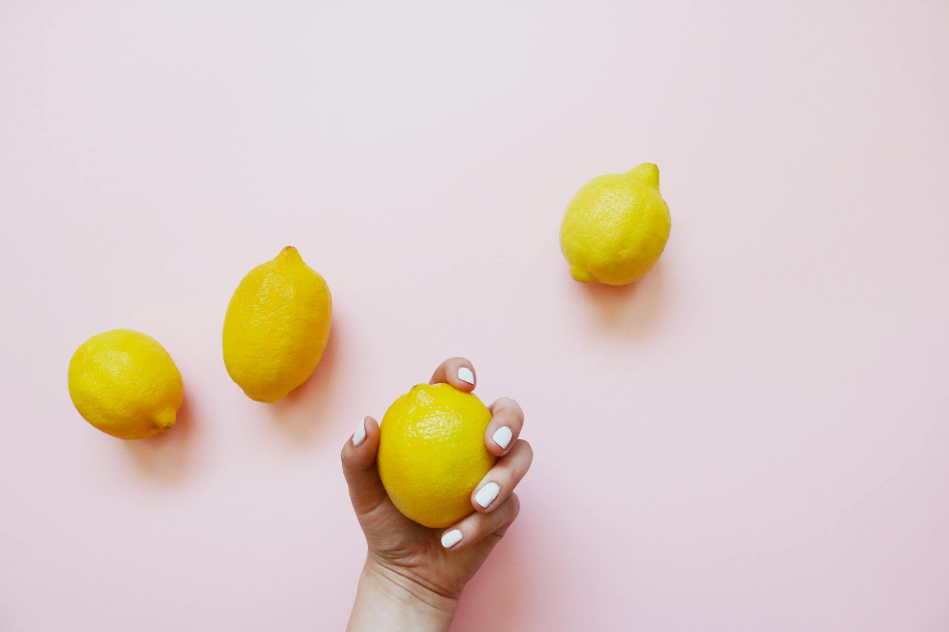 A hand holding a yellow lemon on a soft pink background, symbolizing fresh approaches to intimate reconnection