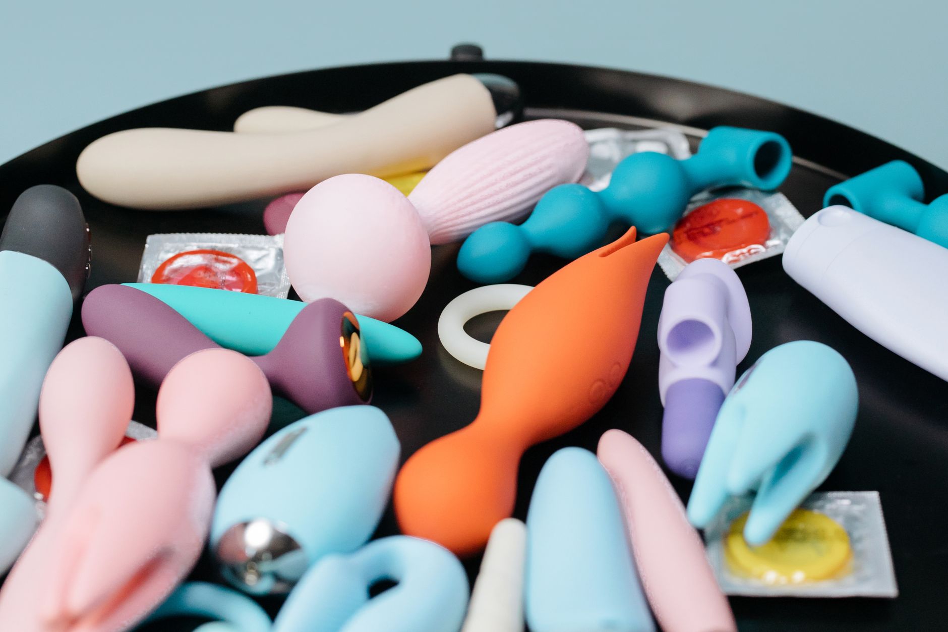 Hands holding pink and blue silicone vibrators against pastel background