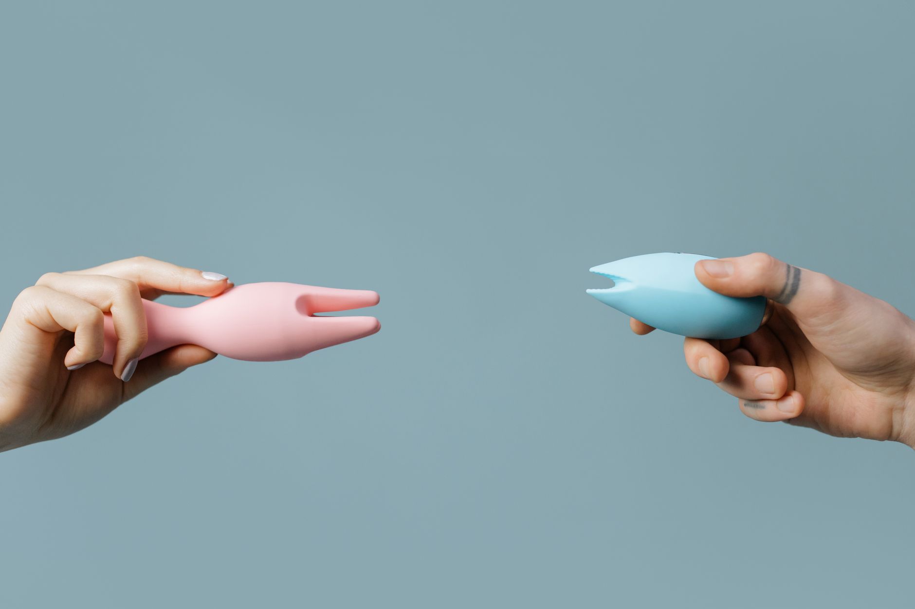 Hands holding pastel-colored silicone sex toys and vibrators.