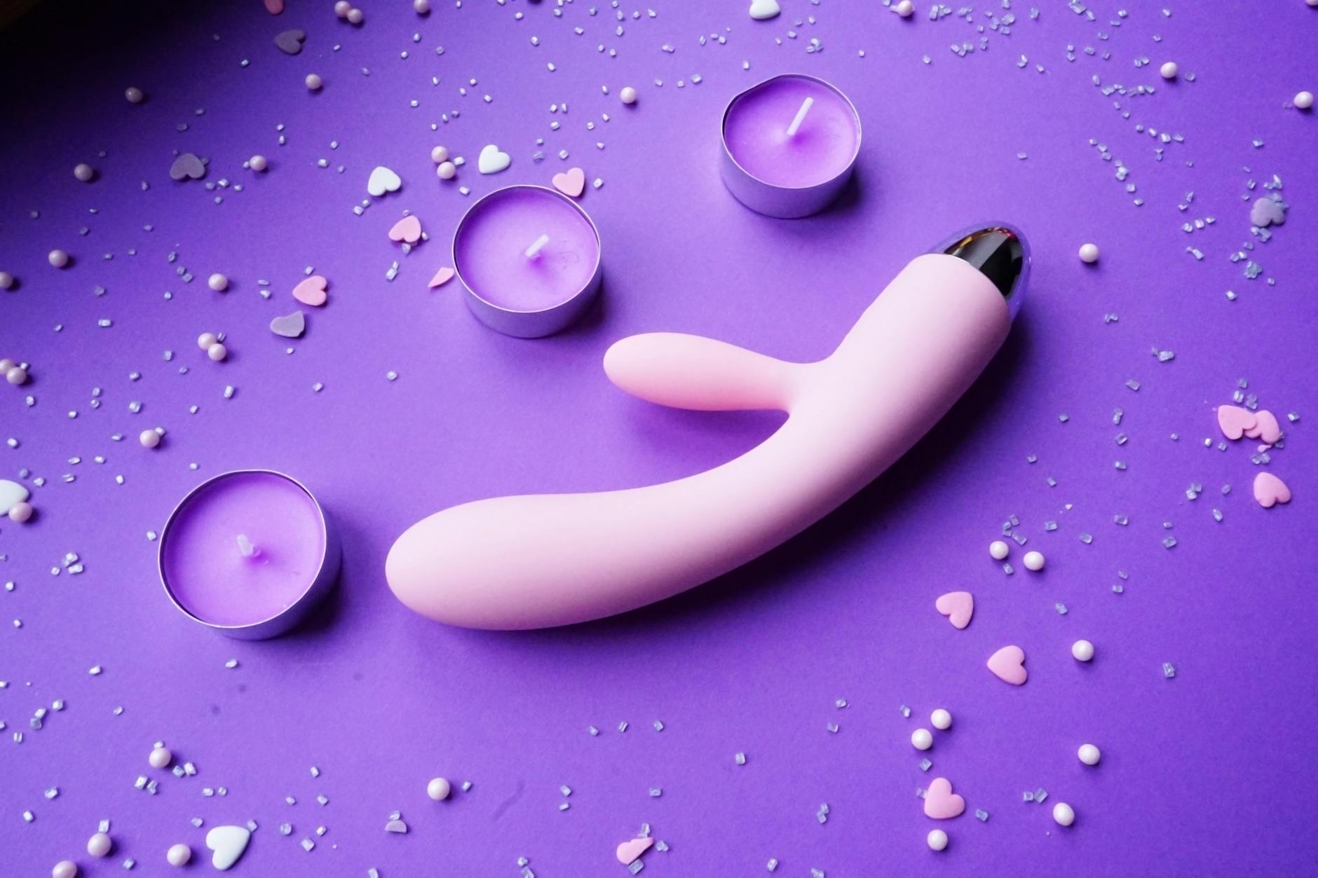 Pink clitoral vibrator on purple background with heart confetti and candles for romantic connection